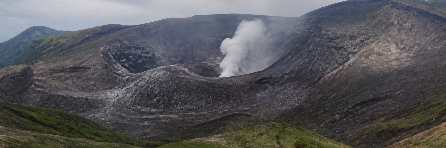 白い噴煙が上がる阿蘇山中岳の火口と周囲の黒い火山地形