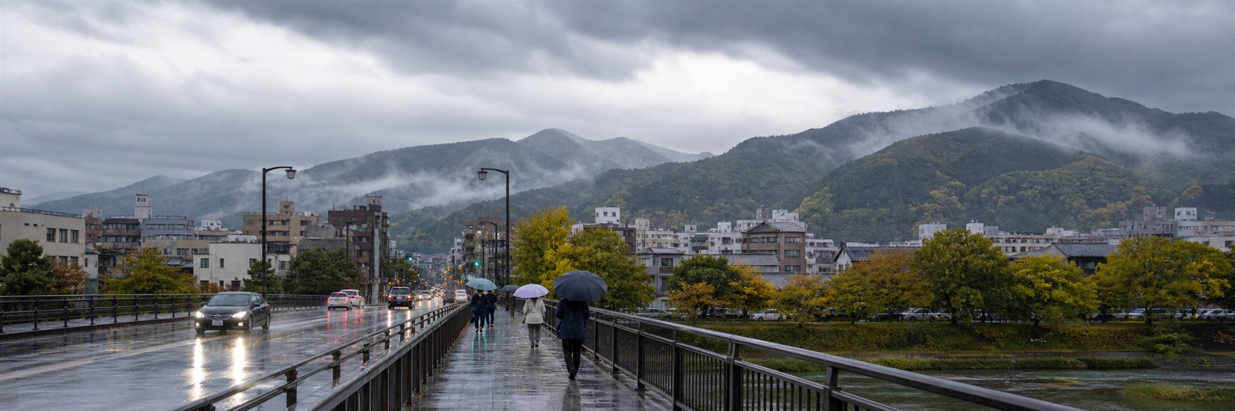 秋雨の雲に覆われた北陸の街と山並みで、濡れた道路を傘を差した人が歩く様子