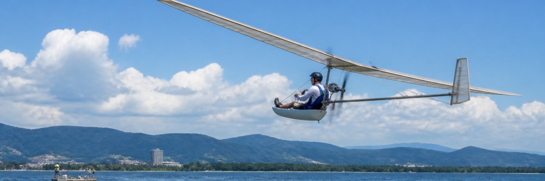 夏の琵琶湖の湖面を、パイロットが操縦する軽量な人力飛行機が低空で飛ぶ様子