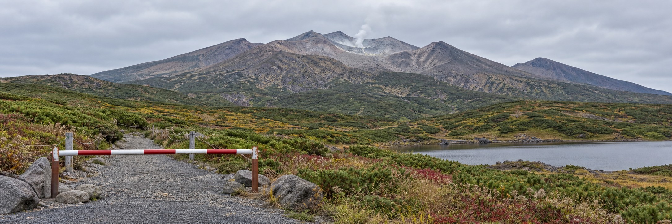 秋の十勝岳を遠方から望み、手前の登山道が赤白の柵で閉鎖された説明用イメージ
