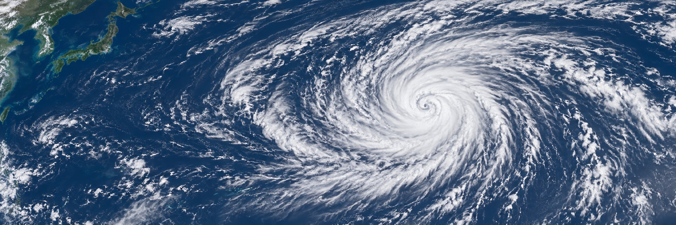 西太平洋上の大型台風を宇宙から見下ろし、広い外側の雲域と遠方の日本列島を示す説明用イメージ